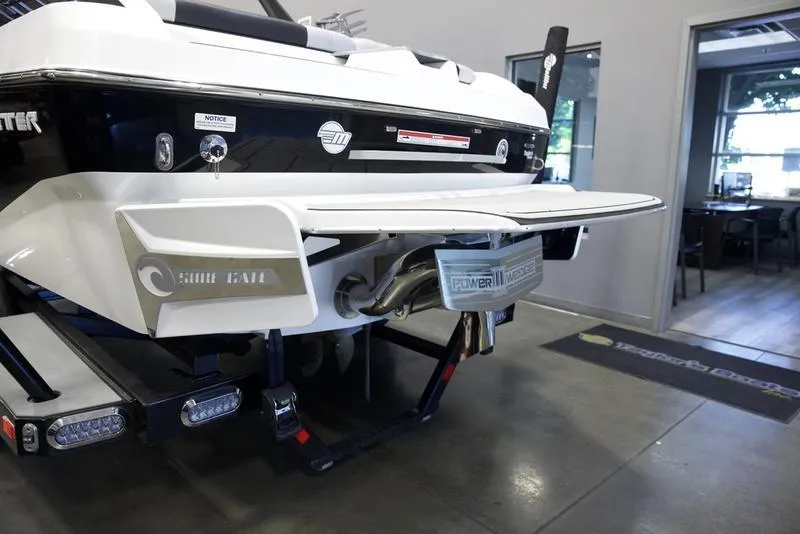 Slide: The Image of 2021 Malibu 21 MLX boat rear view in showroom, showcasing swim platform and exhaust system. - 3