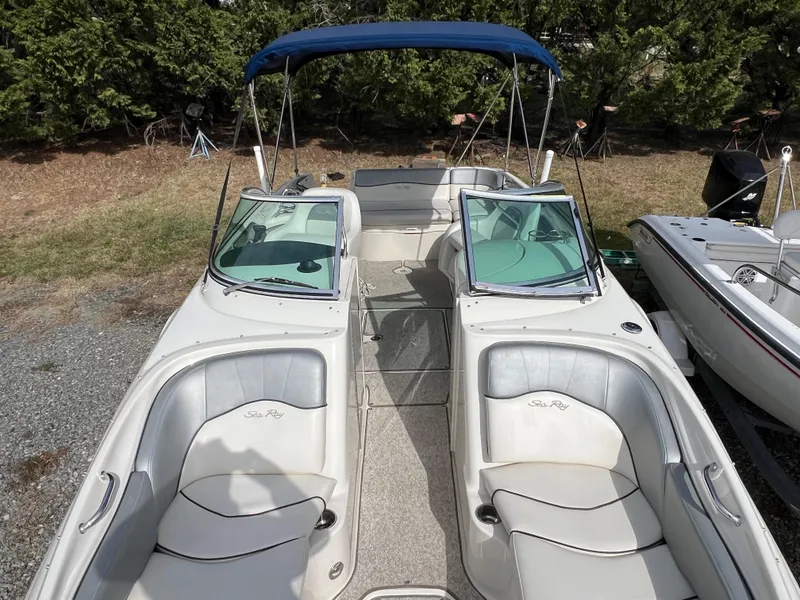 Slide: The Image of 2009 Sea Ray 240 Sundeck boat with blue canopy, parked on gravel near trees. - 10