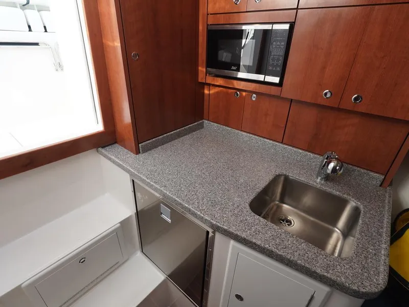 Slide: The Image of 2024 Albemarle 30 Express boat kitchen with sink, microwave, and wooden cabinetry. - 9
