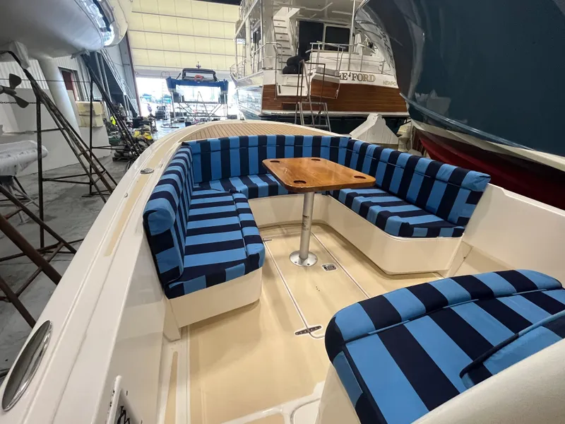 Slide: The Image of 2021 Vanquish 26 boat with blue-striped seating and wooden table in a marina setting. - 9