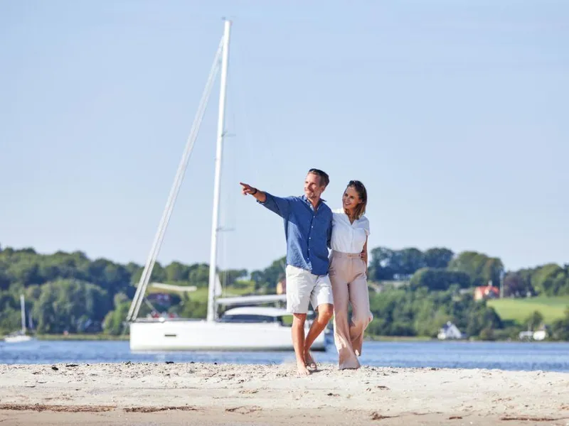 Slide: The Image of Couple walking on beach with 2025 Moody 41 DS sailboat in background. - 4