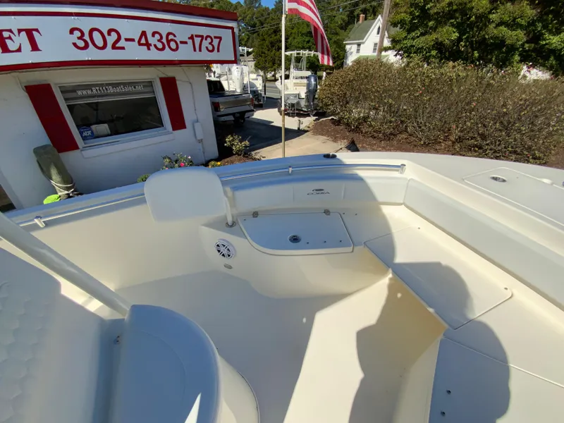Slide: The Image of 2025 Cobia 220 Center Console boat at dealership, sunny day, American flag in background. - 13