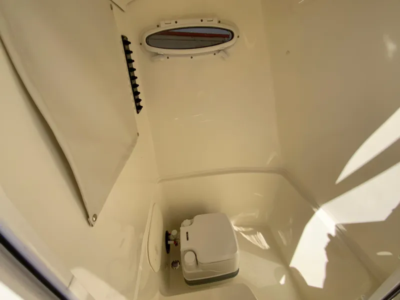 Slide: The Image of 2025 Cobia 220 Center Console boat interior with compact toilet and small window. - 18