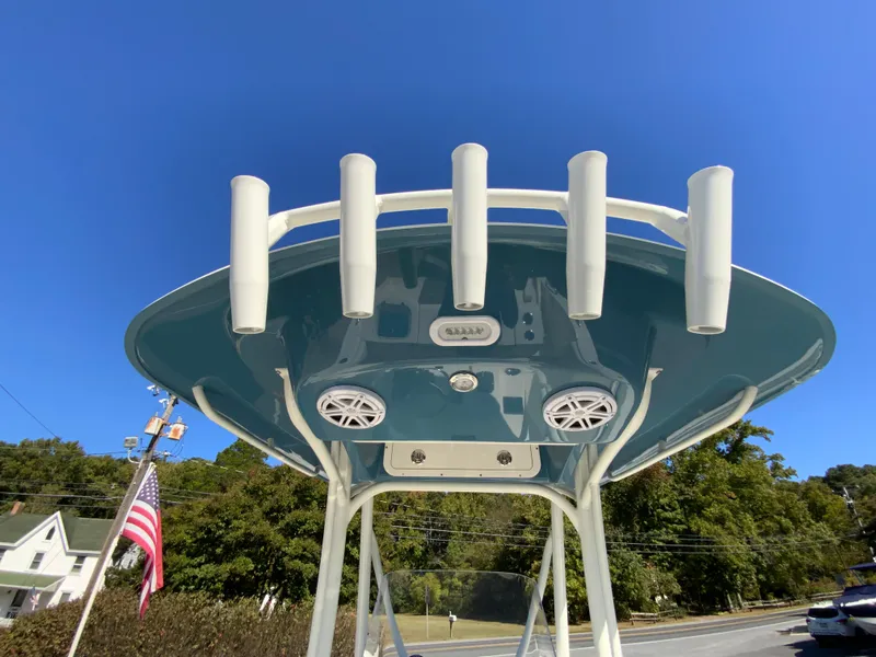 Slide: The Image of 2025 Cobia 220 Center Console boat with rod holders and speakers, under clear blue sky. - 23