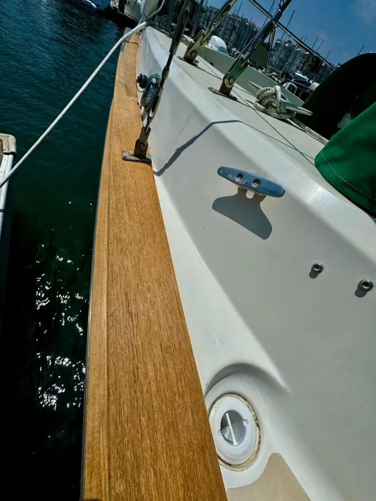 Slide: The Image of 1982 Pearson Ketch sailboat deck with wooden trim and cleat, docked in marina. - 16