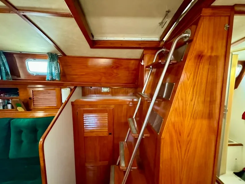 Slide: The Image of Interior of 1982 Pearson Ketch sailboat with wooden stairs and green seating. - 32