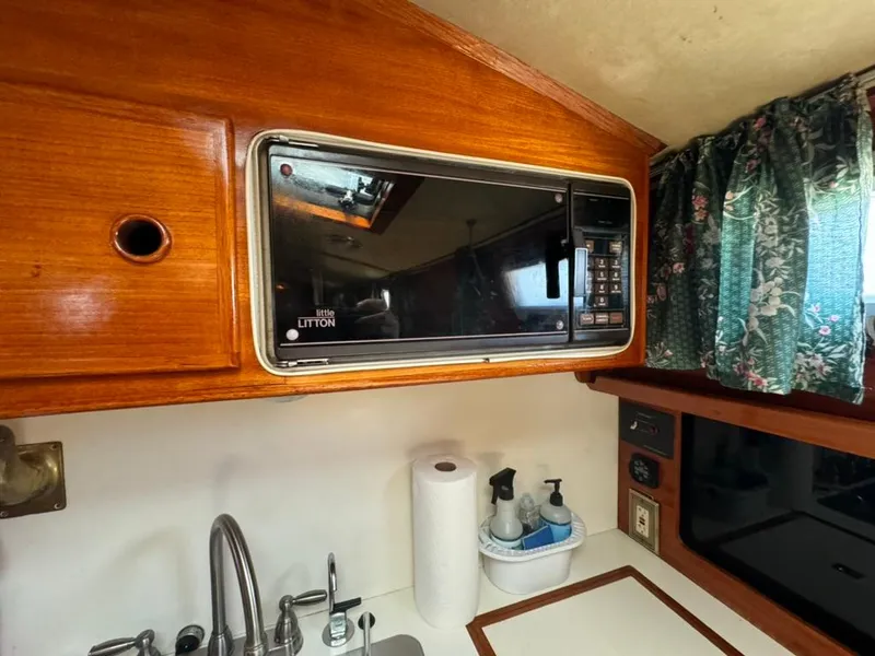 Slide: The Image of 1982 Pearson Ketch galley with microwave, sink, and floral curtains. - 48