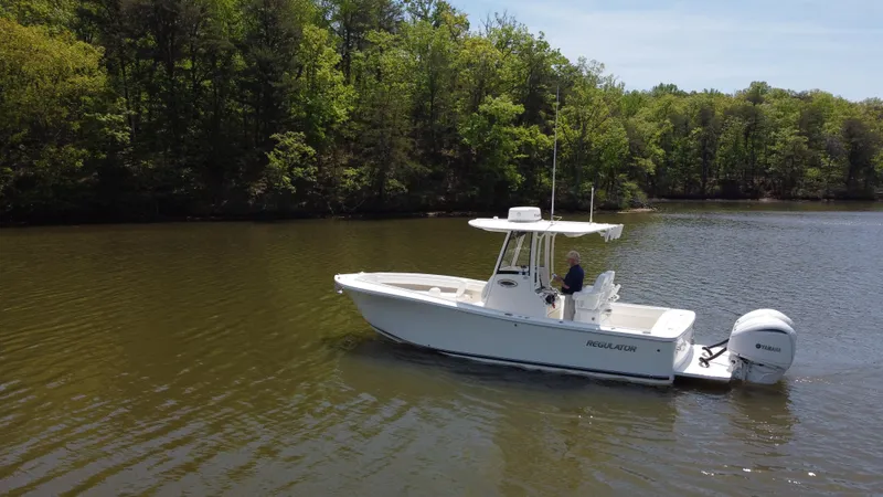 Slide: The Image of 2022 Regulator 25FS boat cruising on a calm lake surrounded by lush trees. - 8
