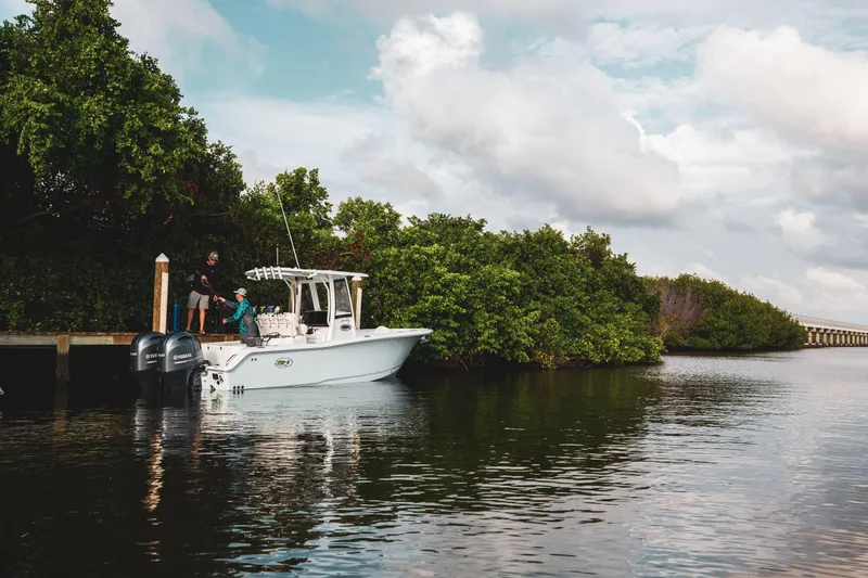 Slide: The Image of 2025 Sea Hunt Gamefish 25 boat docked by lush greenery under cloudy sky. - 9