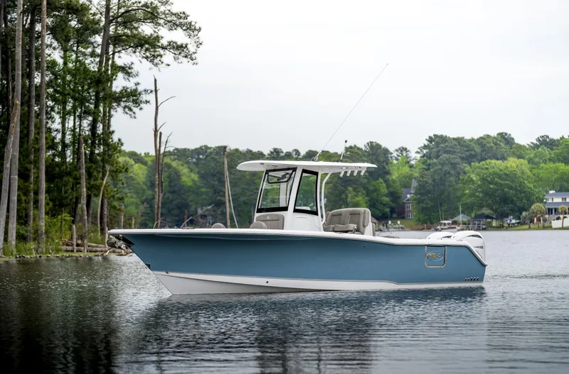 Slide: The Image of 2025 Sea Hunt Gamefish 27 boat on a serene lake with lush greenery. - 1
