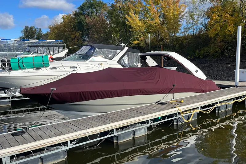 Slide: The Image of 2018 Monterey 328 Super Sport boat docked, covered with a maroon tarp, surrounded by autumn trees. - 2