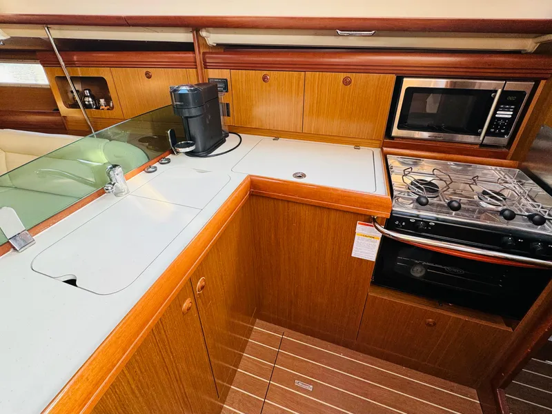 Slide: The Image of 2007 Jeanneau Sun Odyssey 36i yacht kitchen with stove, microwave, and wooden cabinetry. - 28