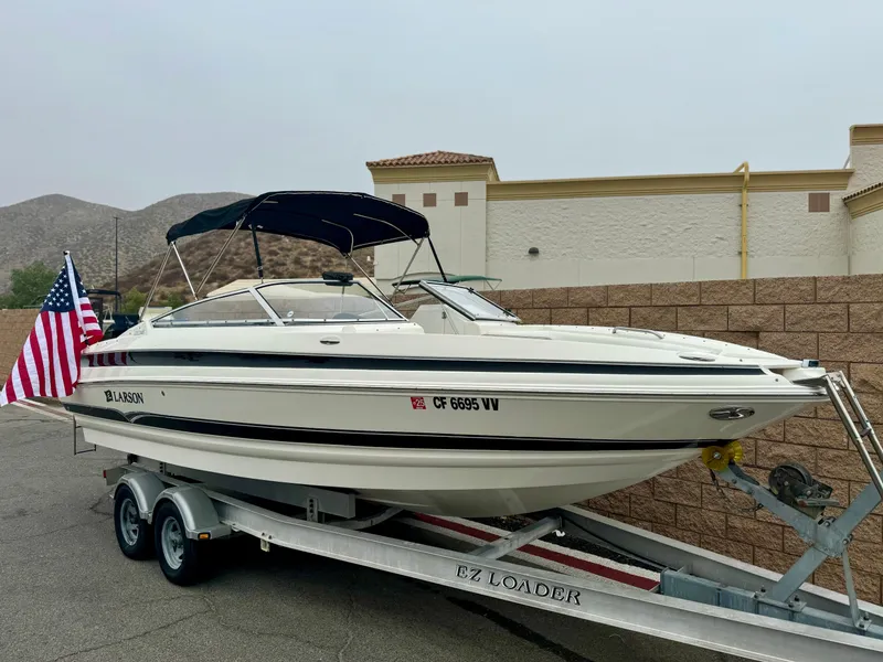 Slide: The Image of 2006 Larson LXi 248 boat on trailer, parked outdoors with mountains in background. - 1