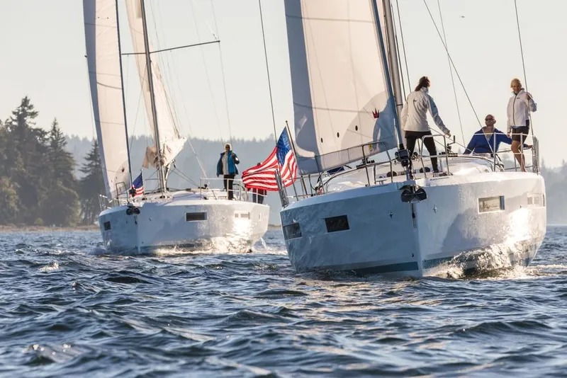 Slide: The Image of 2024 Jeanneau Sun Odyssey 490 sailboats on open water, with crew and American flags. - 49
