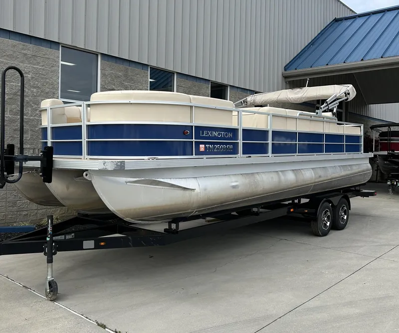 Slide: The Image of 2018 Lexington 325 Sport Tri-Toon boat on trailer outside a building. - 1
