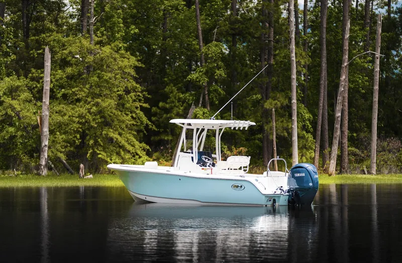 Slide: The Image of 2025 Sea Hunt Ultra 229 boat on a serene lake with lush forest backdrop. - 17