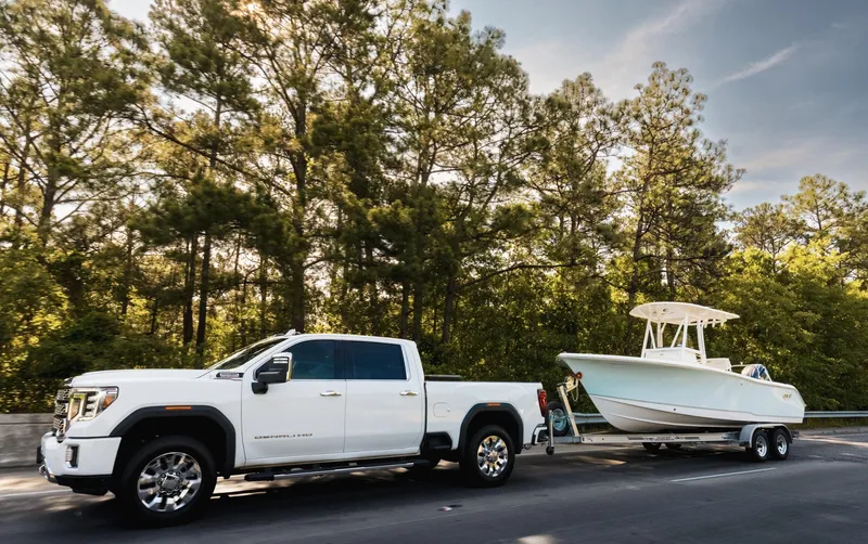Slide: The Image of White truck towing 2025 Sea Hunt Ultra 229 boat on a forested road. - 2
