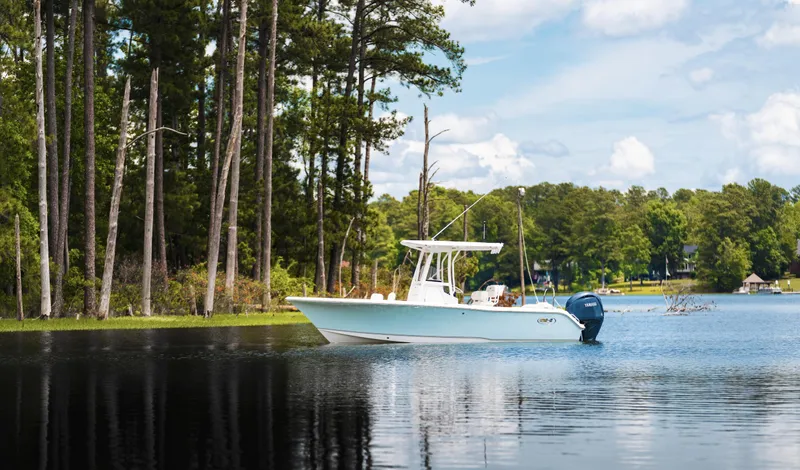 Slide: The Image of 2025 Sea Hunt Ultra 229 boat on a serene lake with forest backdrop. - 23