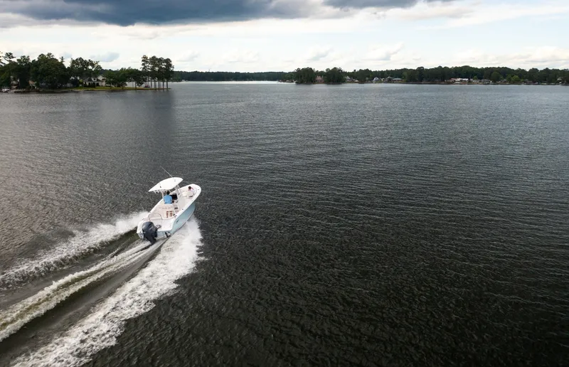 Slide: The Image of 2025 Sea Hunt Ultra 229 boat cruising on a serene lake under cloudy skies. - 25