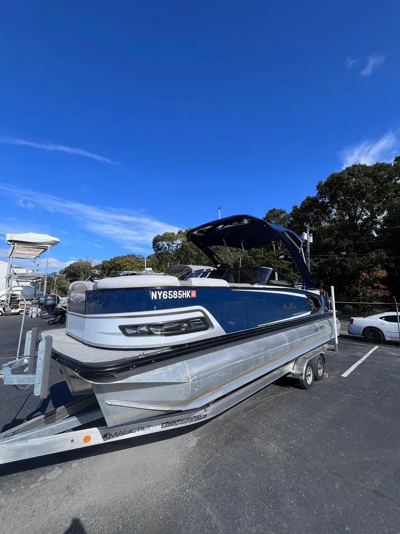 The Image of 2023 Avalon Excalibur Elite Windshield boat on trailer under clear blue sky. - 0