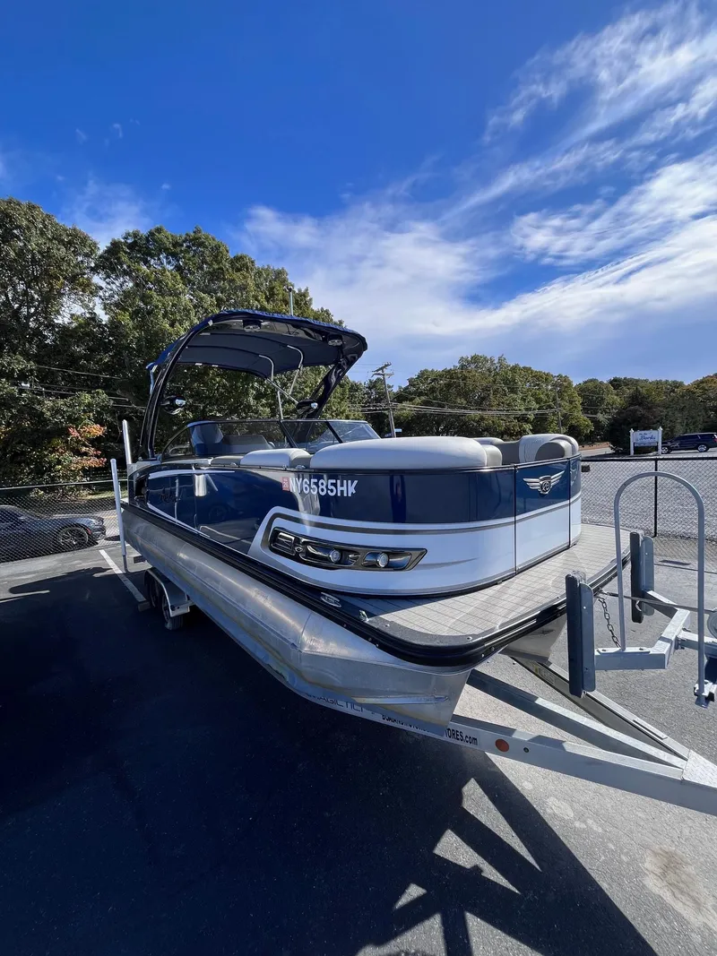 Slide: The Image of 2023 Avalon Excalibur Elite Windshield boat on trailer under clear blue sky. - 5