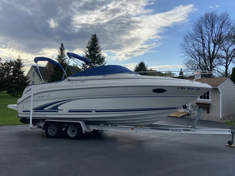 Slide: The Image of 2000 Sea Ray 245 Weekender boat on trailer in driveway, under cloudy sky. - 1