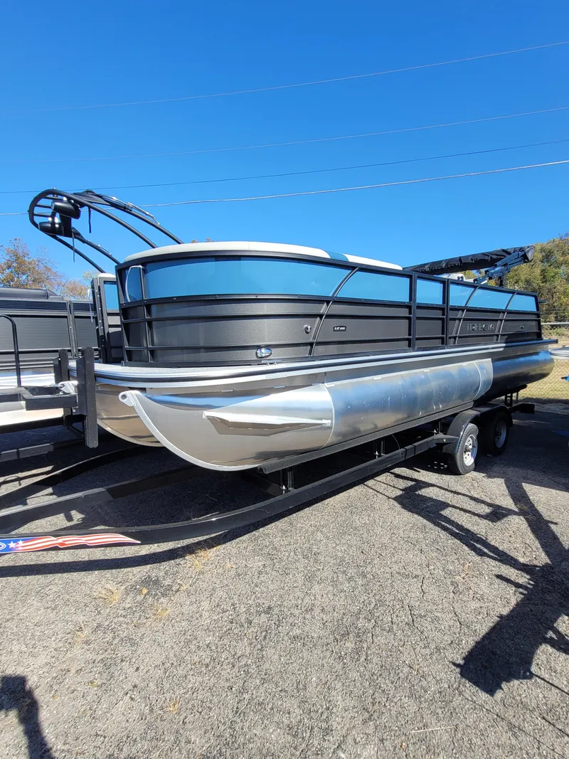 Slide: The Image of 2025 Trifecta 24ULLET275 pontoon boat on trailer, sleek design, parked outdoors. - 1