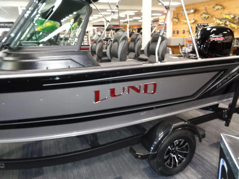 Slide: The Image of 2025 Lund 1875 Impact XS Sport boat displayed indoors, featuring sleek design and modern seating. - 11