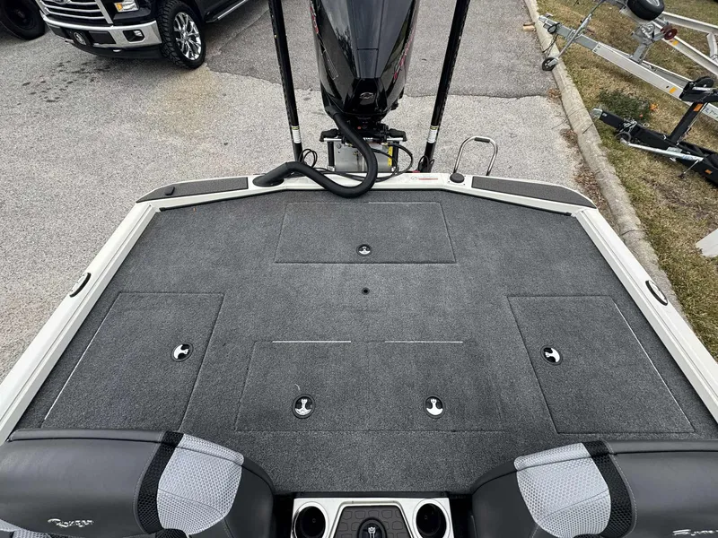 Slide: The Image of 2025 Ranger ALPHA 208 boat deck with storage compartments and motor, parked on pavement. - 6