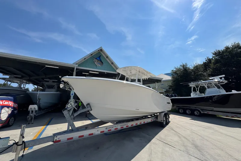 Slide: The Image of 2024 NauticStar 292 Legacy boat on trailer, parked outside a marina under a clear sky. - 4