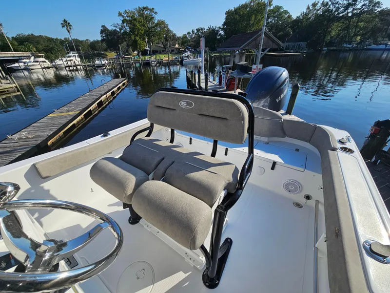 Slide: The Image of 2025 Sea Hunt Ultra 229 boat interior with seating, docked by a scenic waterfront. - 16