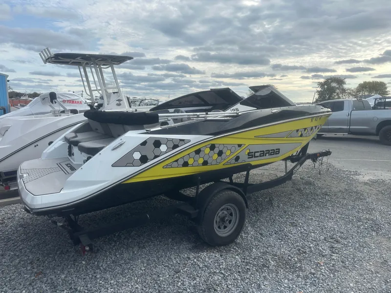 Slide: The Image of 2020 Scarab 195 ID boat on trailer, yellow and black design, parked on gravel. - 5