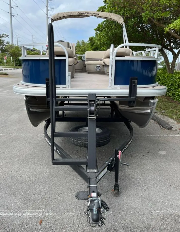 Slide: The Image of 2025 Sun Tracker Bass Buggy 18 DLX pontoon boat on trailer in parking lot. - 2