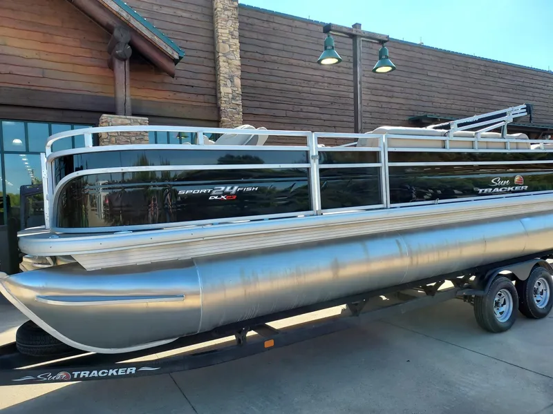 Slide: The Image of 2025 Sun Tracker Sportfish 24 XP3 pontoon boat on trailer, parked outdoors. - 2