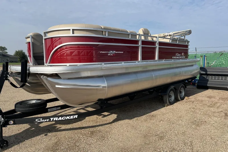 The Image of 2025 Sun Tracker Party Barge 22 XP3 pontoon boat on trailer, red and beige design. - 0