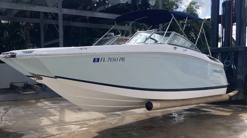 Slide: The Image of 2013 Cobalt 24SD boat on lift, white hull, blue canopy, dockside view. - 3