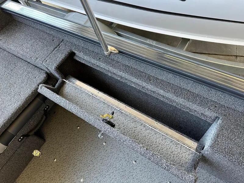 Slide: The Image of 2025 Lund 1775 Adventure Sport boat interior storage compartment, featuring carpeted finish and metal trim. - 20