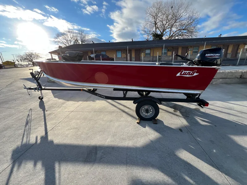 Slide: The Image of 2025 Lund 1600 Fury Tiller boat on trailer, red exterior, sunny day. - 2