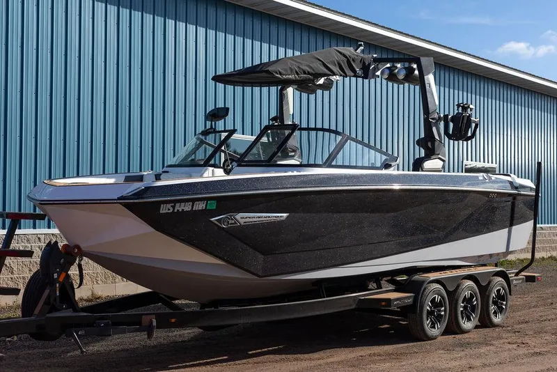 Slide: The Image of 2022 Nautique Super Air Nautique G25 boat on trailer, parked by blue building. - 1