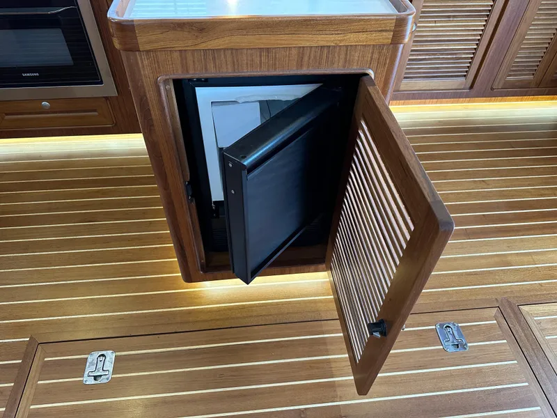 Slide: The Image of 2023 Helmsman Trawlers 43E PILOTHOUSE interior with open wooden cabinet and refrigerator. - 22