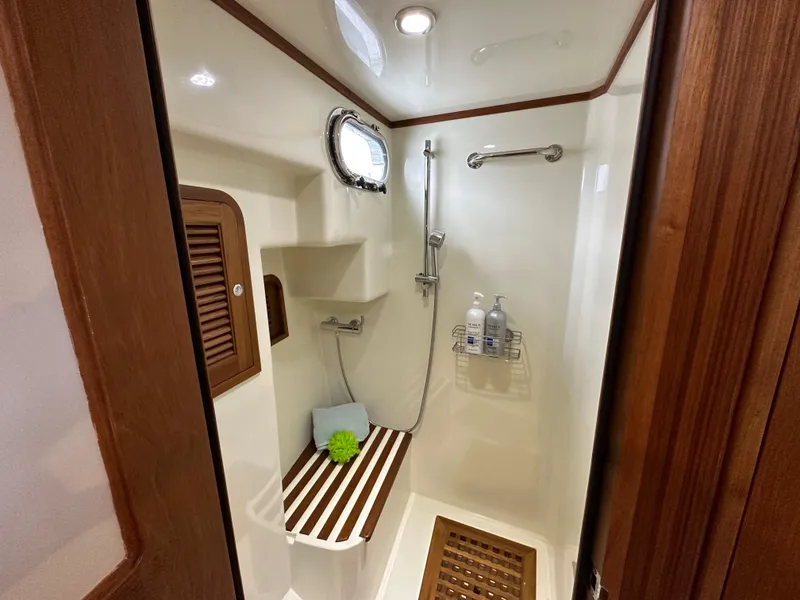 Slide: The Image of 2023 Helmsman Trawlers 43E PILOTHOUSE bathroom with shower, wooden accents, and porthole window. - 30