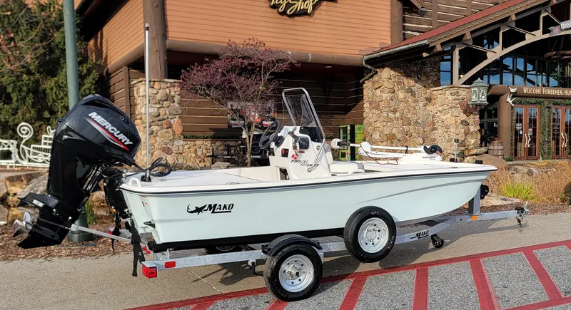 Slide: The Image of 2025 Mako Pro Skiff 13 CC boat on trailer, parked outside rustic building. - 0