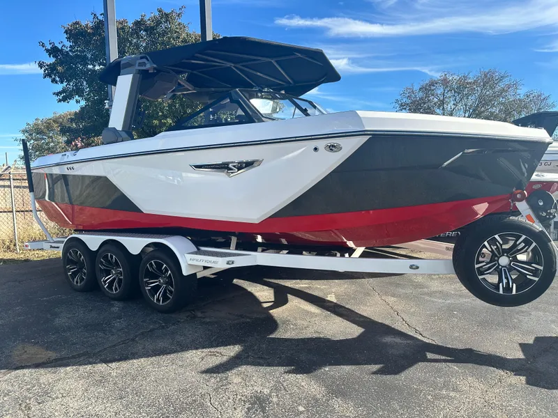 Slide: The Image of 2022 Nautique S23 boat on trailer, white and red design, parked outdoors. - 1