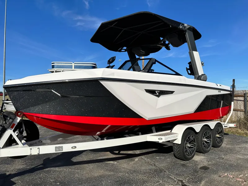 Slide: The Image of 2022 Nautique S23 boat on trailer, black and red design, under clear blue sky. - 2