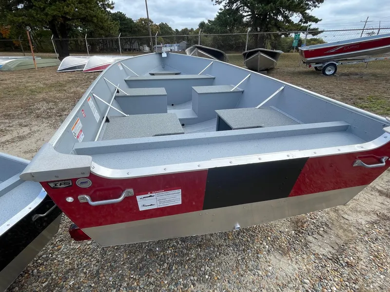 Slide: The Image of 2025 Lund SSV-16 Tiller boat, red and silver, parked outdoors on gravel. - 2