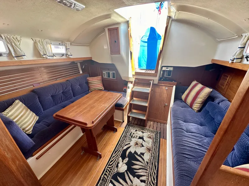 Slide: The Image of 1986 Nonsuch Ultra yacht interior with blue seating, wooden table, and floral rug. - 2