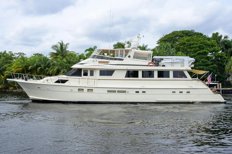 Slide: The Image of 1991 Hatteras 78 CMY yacht cruising on a serene waterway with lush greenery. - 8
