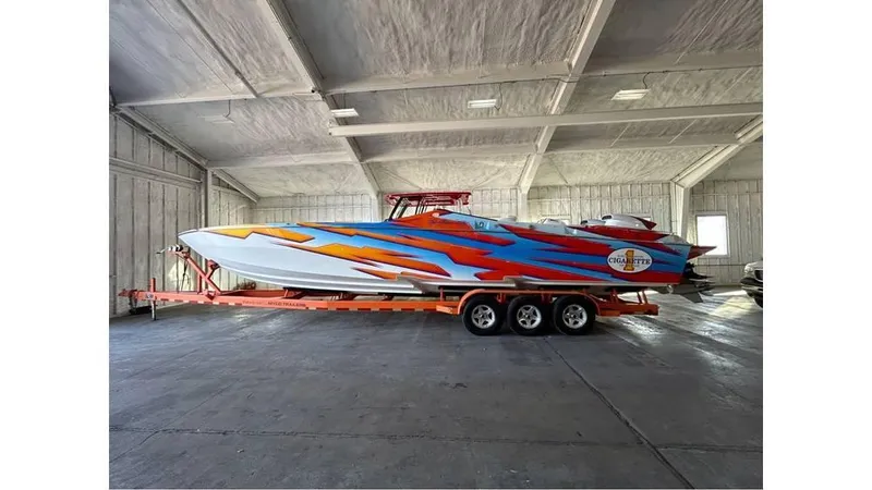 The Image of 2003 Cigarette 38 Top Gun boat with vibrant paint, stored indoors on a trailer. - 0