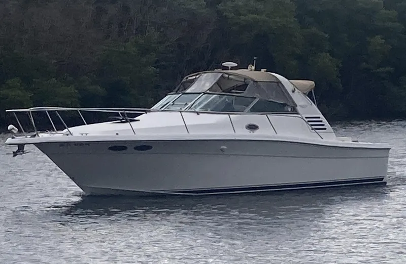 Slide: The Image of 1999 Sea Ray 330 Express Cruiser on calm water, surrounded by lush greenery. - 0