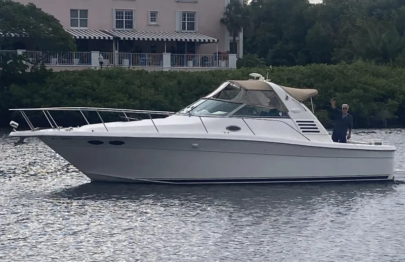 Slide: The Image of 1999 Sea Ray 330 Express Cruiser on calm water, with lush greenery in the background. - 1